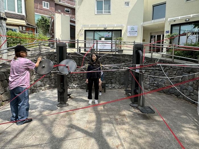 Performers among exercise equipment connected by red and white thread in an urban pocket space