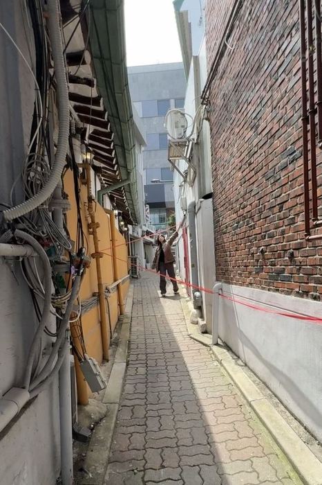 A performer connecting the surfaces of a narrow alley with red thread