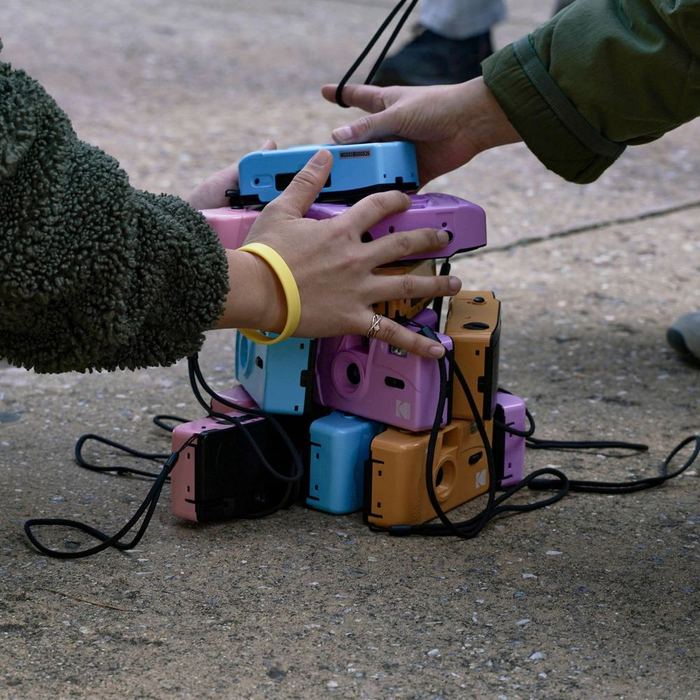 Hands gathering a stack of colourful cameras during Traces of the Unseen